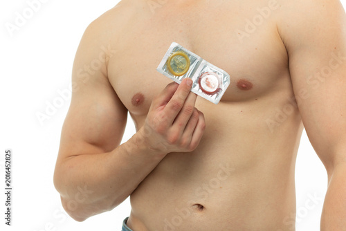 Slika na platnu A young guy with an athletic figure and a prominent torso is holding a condom in his hands