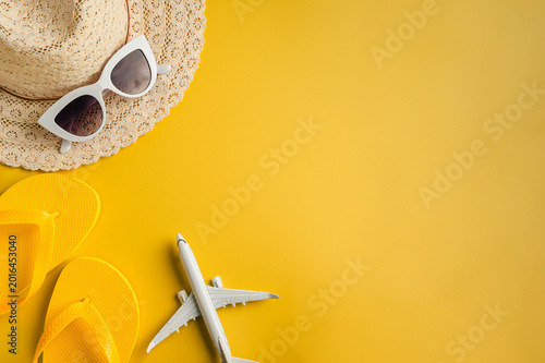 Travel-themed flat lay, summer holiday background. Toy model airplane, sunglasses, sun hat over yellow backgrounds, copy space