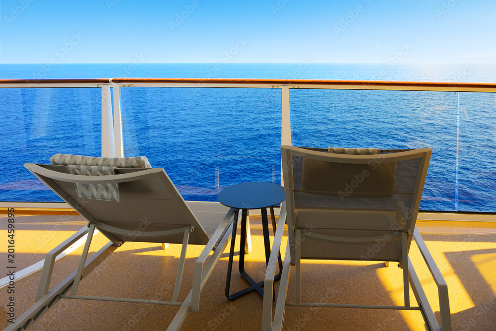 Fototapeta premium Two reclining lounge chairs on a private stateroom balcony of a cruise ship cabin overlooking the blue Mediterranean Sea.
