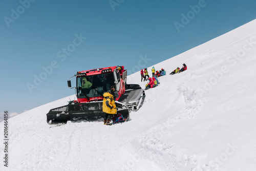 Foto Group of mountaineers in colorful winter gear resting beside a snowcat on a stee