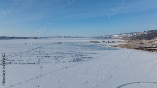 Wide winter view of the frozen Small Sea strait on Lake Baikal with snow-covered ice, distant islands and mountain shoreline under clear blue sky, Russia