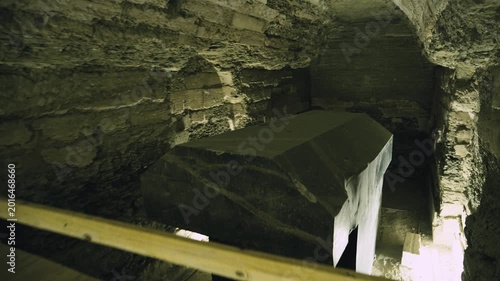 Dark underground corridor with stone arches leading to massive granite sarcophagus inside Serapeum of Saqqara, Egypt, dramatic warm lighting on ancient rock-cut tunnel walls.