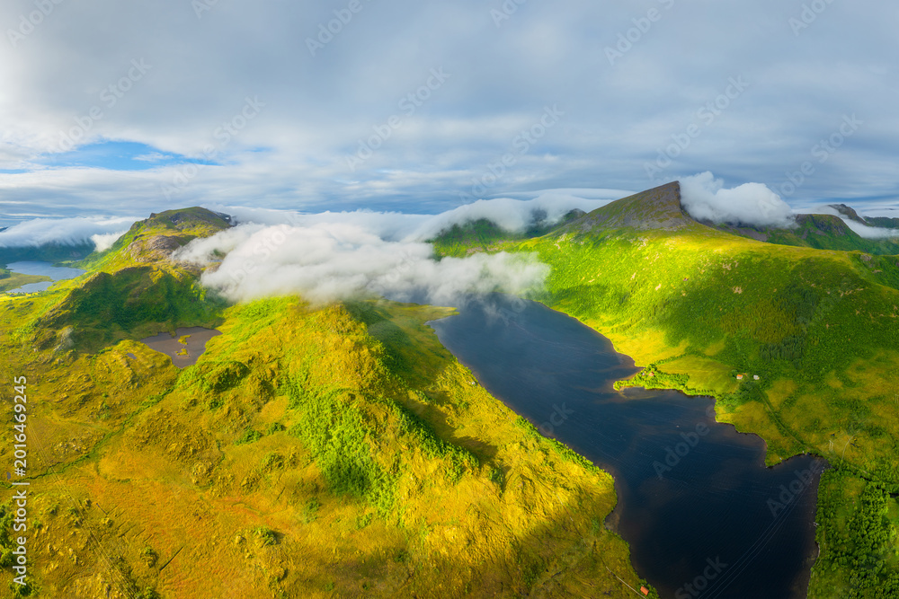 Naklejka premium Aerial view of misty mountains and fjords in Lofoten, Norway. Atmospheric arctic landscape with fog from a drone. Clouds and scenic northern nature. View from above.