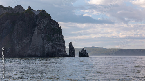 Fotografie Rugged coastal cliffs and sharp sea stacks rising from calm water in Avacha Bay,
