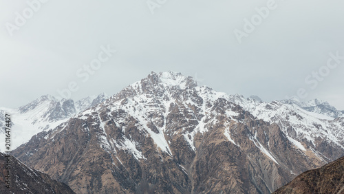 Wide view of snow-covered mountain range and rocky slopes under cloudy sky at Too Ashuu Pass, Chuy Region, Kyrgyzstan, scenic high-altitude landscape