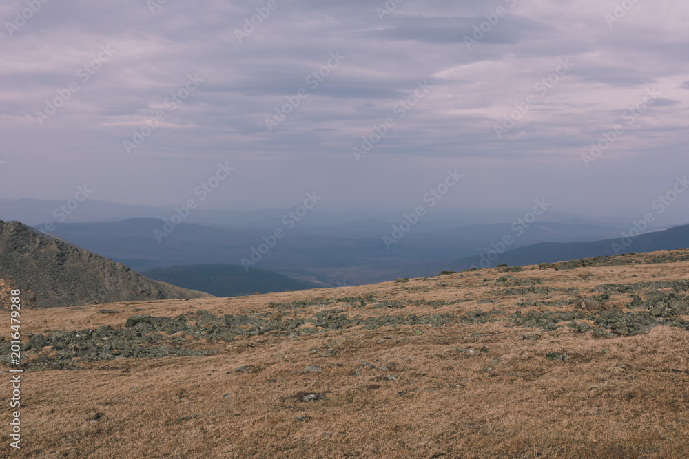 Fototapeta premium Wide panoramic view from Konzhakovsky Kamen of mountain tundra and rocky plateau with layered blue ridgelines and overcast sky, Ural Mountains, Russia