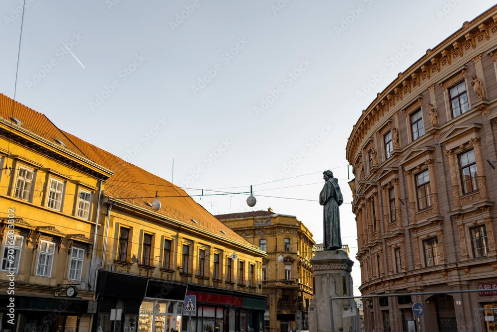 Fototapeta premium Historic Zagreb street with statue and classical architecture during golden hour Croatia