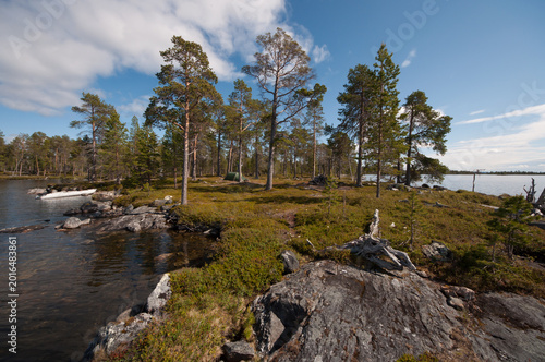 Sunny summer day on an wilderness island on the lake Inari in Lapland, Finland with an inflatable boat and a green tent on the shore