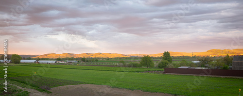 Canvas Print Rural farmland landscape at sunset with rolling hills, green fields and dramatic cloudy sky in Mures valley, central Transylvania, Romania