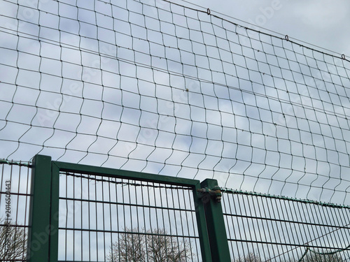 Metal fence with protective netting against cloudy sky