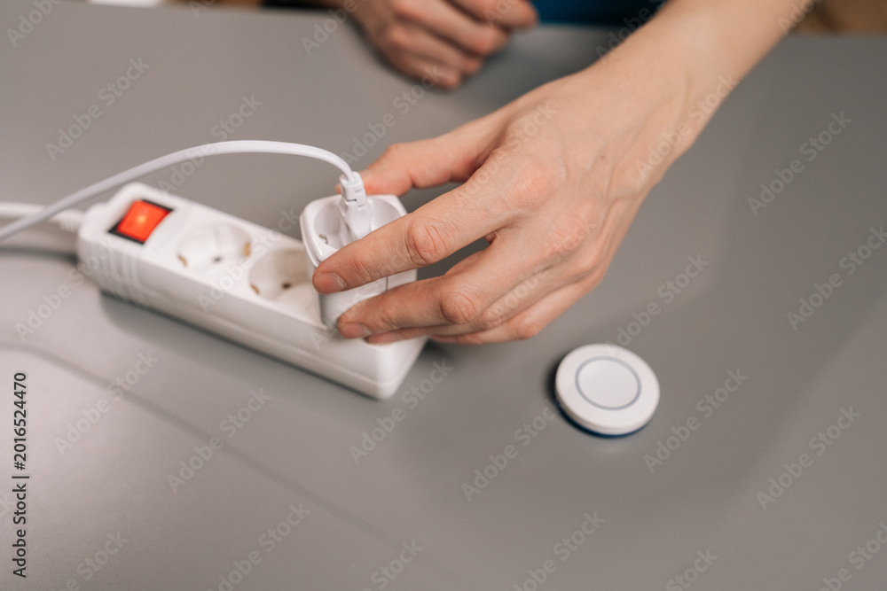 Fototapeta premium Male hands plugging a smart plug into a power strip and pressing its button, illustrating easy setup, remote control, energy saving home automation in a modern indoor setting.