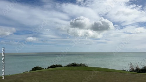 Scenic coastal view with rolling green hills and dramatic clouds over the tranquil ocean, showcasing nature's beauty and serenity