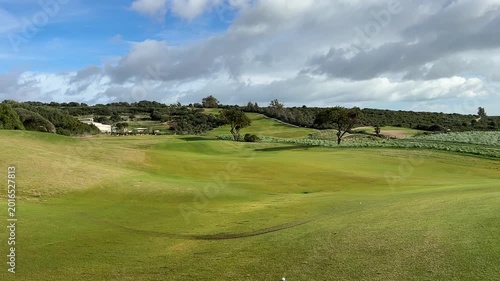 Scenic golf course landscape with rolling hills, lush green grass, and cloudy sky, showcasing natural beauty and tranquility