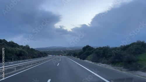 Scenic highway drive through lush green landscape under cloudy sky, showcasing road signs and vehicles in motion