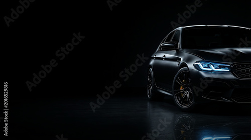 Dark gray luxury sport sedan with glowing blue LED daytime running headlights in dark studio background