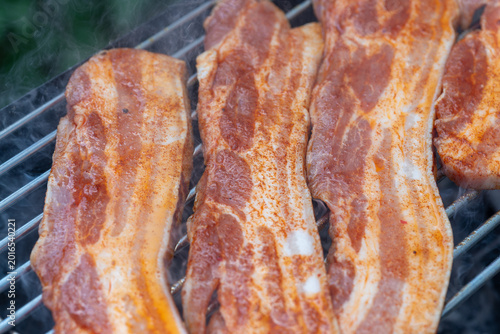 Pork belly slices cooking on barbecue grill with smoke
