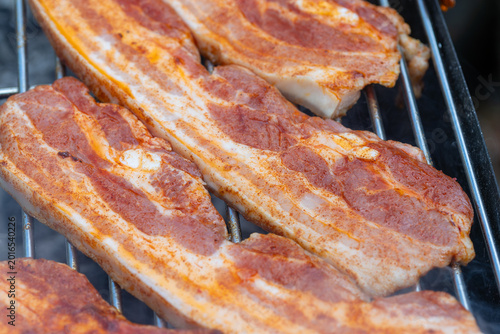 Seasoned pork belly slices grilling on a barbecue grate