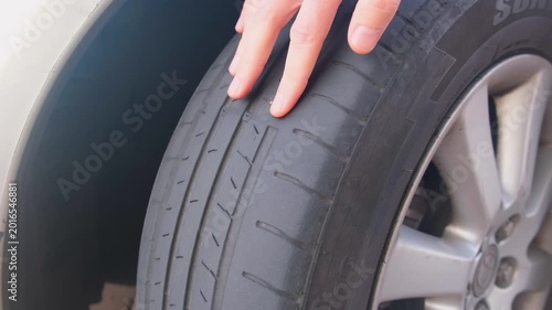 Close-up of a hand pointing at a worn and damaged car tire, checking for safety