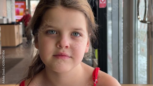 Young girl with brown hair in red dress gazes thoughtfully out of a cafe window, capturing a moment of contemplation and curiosity