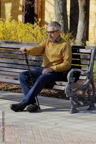 Valokuva An elderly pensioner dozes off with a walking-stick in his hand while sitting on a bench in a park
