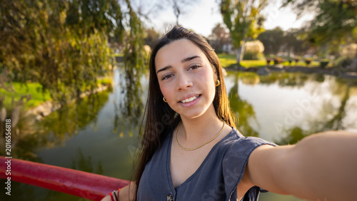 Young woman smiling while taking a selfie on a bridge in a park