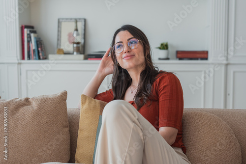 Foto Young woman in glasses lounging on a cozy sofa at home, smiling and gazing upwar