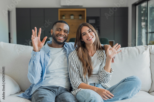 Tableau sur toile Happy multi-ethnic couple relaxing on a white sofa in their modern living room,