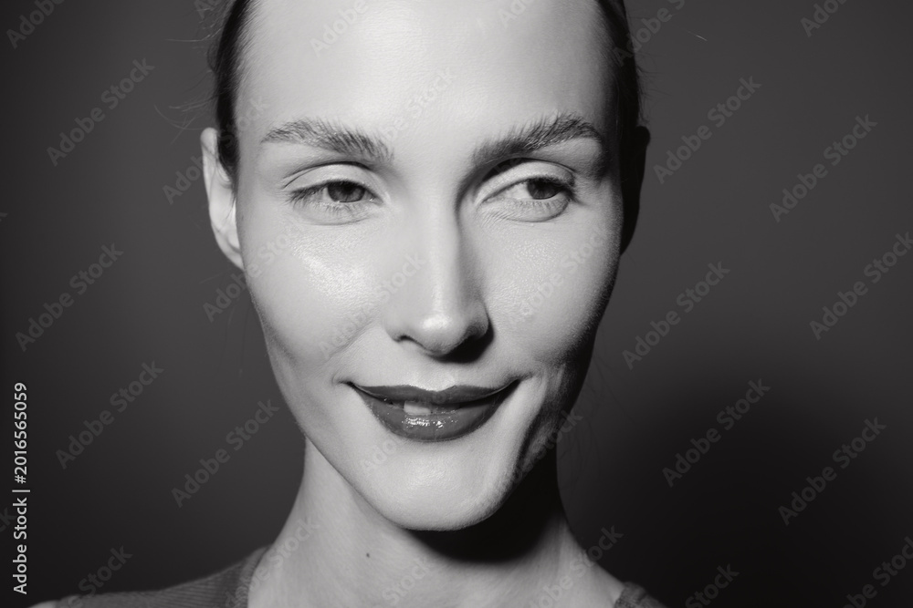 Fototapeta premium Close-up portrait of a young white woman with pale skin smiling softly. Black and white studio photo emphasizing natural beauty and subtle positive emotion in monochrome.