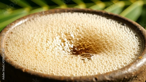 Close up of frothy beverage in rustic ceramic cup with palm leaves background.