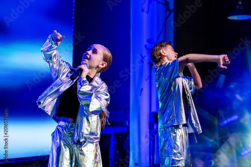 Girl and boy dancing on stage under stage light. Young dancers performing in shiny costume. Music show concert