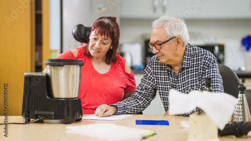 Bild auf Leinwand Woman with disability and senior man cooking together in kitchen, using a smart