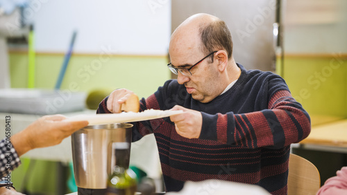 Man with disability carefully grating food into appliance, focusing on cooking during a daily life skill activity