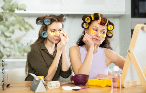 Schilderij op canvas Adult and young women curl their hair with curlers and use hydrogel eye patches