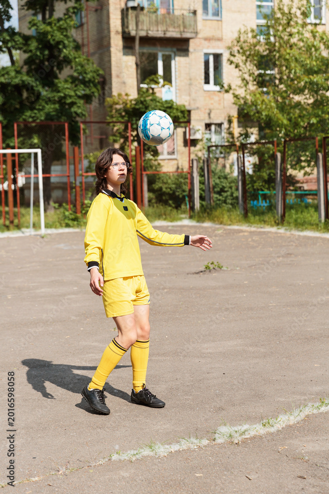Obraz premium Teenage boy soccer player watching ball in air during outdoor training on residential playground