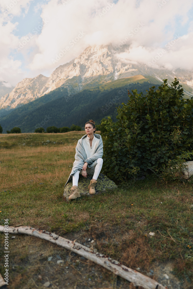 Obraz premium Woman sitting outdoors in a mountain landscape, lifestyle portrait with calm mood, wearing a light jacket and boots, amid natural scenery and clear sky