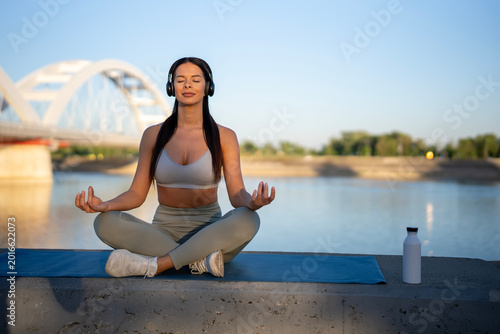 Quadro em tela Woman meditating outdoor wearing headphones by river