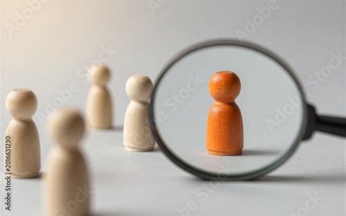 Magnifying glass highlights one orange wooden figure among beige