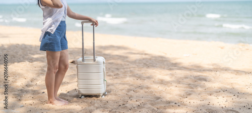 Asian happy woman tourist in summer hat standing barefoot holding luggage arriving at tropical beach, Beautiful female traveler enjoying sunny holiday vacation and travel, resort and hotel arrival