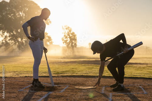 Foto Two men standing on baseball diamond at dusk, one wearing helmet adjusting home