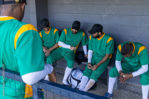 Photography Diverse male baseball players sitting on dugout bench, wearing green uniforms, h