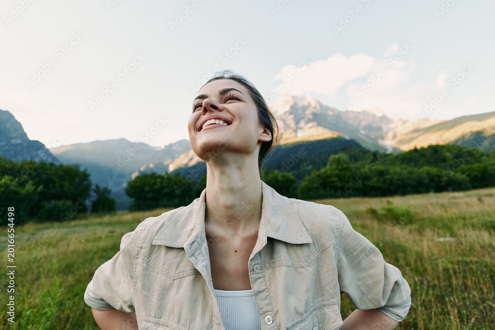 Naklejka premium Young woman with short hair enjoys fresh mountain air with closed eyes and a smile while standing in a green meadow under a clear sky.