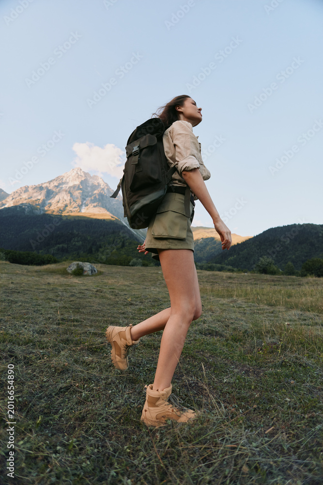Fototapeta premium A woman hiking outdoors with a backpack in a mountainous landscape, wearing shorts and boots. A lifestyle moment of adventure, exploration, and outdoor fitness in nature.