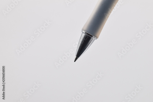 Close-up photograph of a ballpoint pen tip suspended over a clean white background, evoking themes of writing, office work, minimal design, creativity and precision for editorial and commercial use.