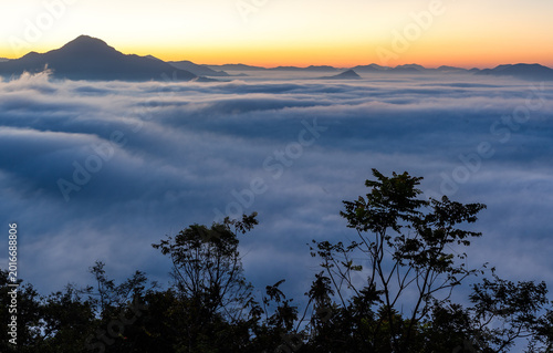 Phu Thok mountain at sunrise. Sea of mist over Chiang Khan, Thailand. Morning light over foggy landscape with trees and hills.