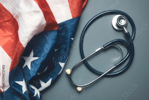 Stethoscope on Grey Background Next to Crumpled American Flag Representing United States Healthcare System and Medical Policy