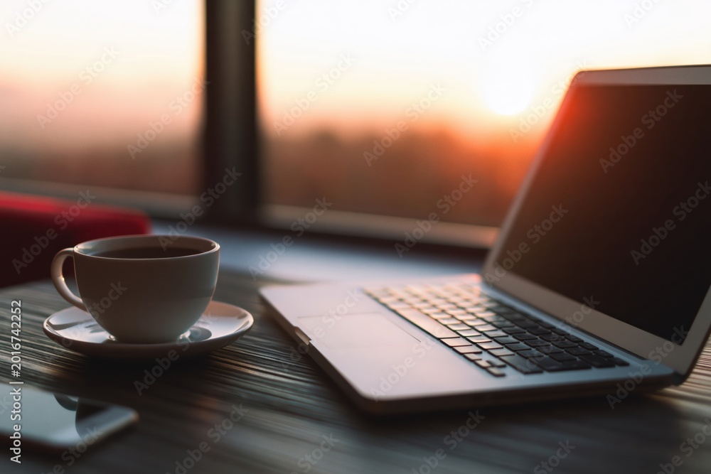 Obraz premium Laptop and coffee cup on table during sunrise