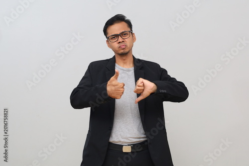 Фотография The young male businessman gave a thumbs up and down, showing an expression of disapproval and approval, an inner conflict