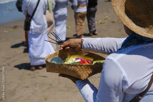 Balinese Woman in White Clothing Carrying Large Woven Basket with Incense, Offerings and Flowers