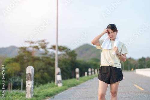 Foto Exhausted Asian woman wiping sweat with a towel after jogging in the park
