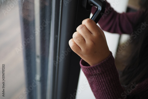 Fotografie Child's hand holds window handle in indoor space